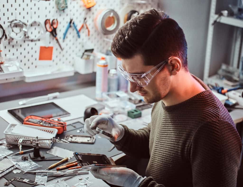 Le technicien utilise une loupe pour inspecter soigneusement les pièces internes du smartphone dans un atelier de réparation mobile. tions internes d'un smartphone dans un atelier de réparation mobile.
